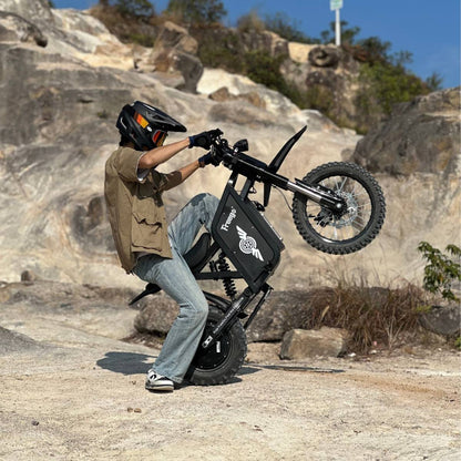 Helmeted rider doing a wheelie on a Freego-branded X0 electric mini dirt bike, set on sunlit rocky terrain.