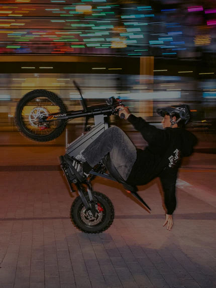 Vertical mobile lifestyle shot of rider doing one-hand wheelie stunt on Freego X0 electric bike, blurred neon colorful city night background