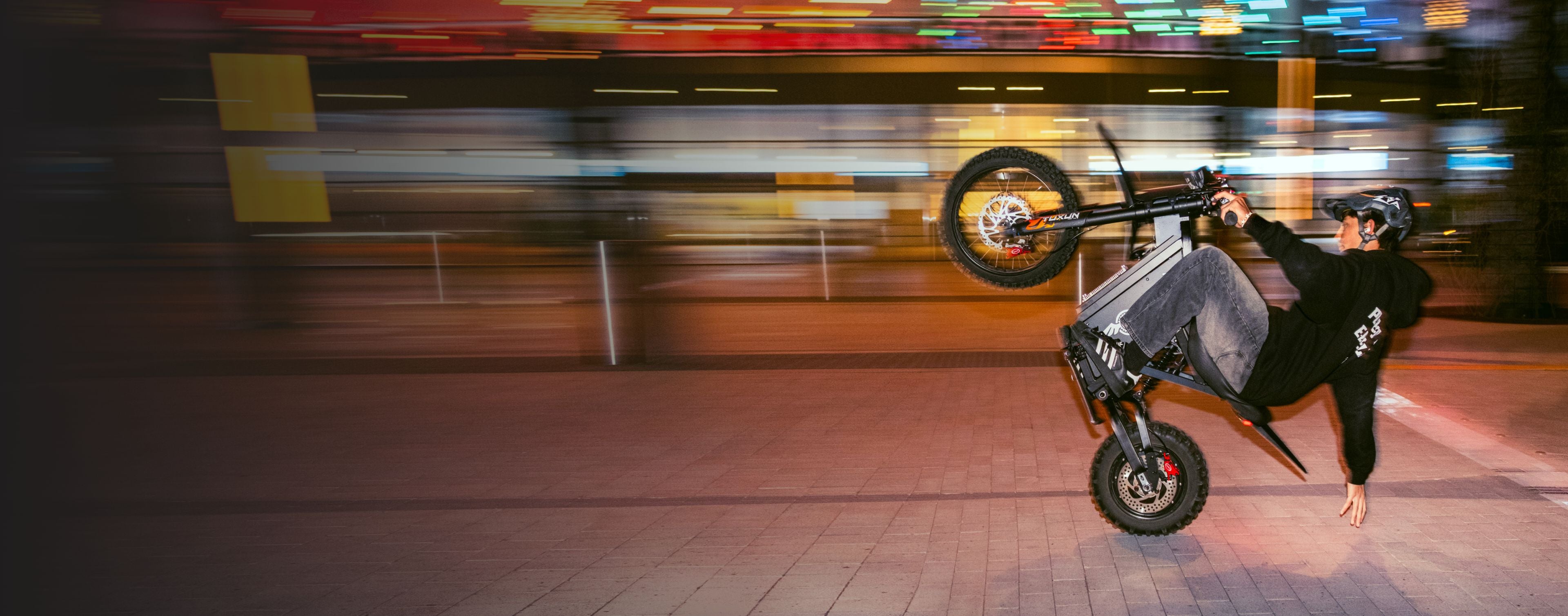 Wide horizontal web banner action shot of rider performing wheelie stunt on Freego X0 electric bike, motion blur neon city night street background