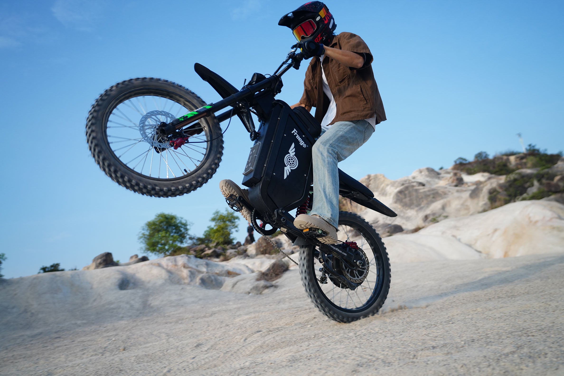 A rider performing a wheelie on the Freego X3 electric dirt bike across rocky terrain, showcasing its powerful performance, rugged off-road design, and thrilling adventure riding experience.